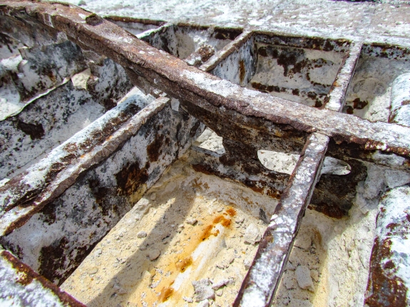Large-format photograph: Close-up view of a removed Crawlerway Grid Panel, showing Top Chord construction (and corrosion damage) in area where concrete fill has been chipped out of the Panel with enough detail visible to determine that the Panels, as originally fabricated and installed, did not match the as-built contract drawings which were submitted and approved at the time (1960's), resulting in a condition where subsequent modifications work would become especially difficult, resolving the discrepant conditions in a timely manner, to everyone's satisfaction. Photo credit: Withheld by request.